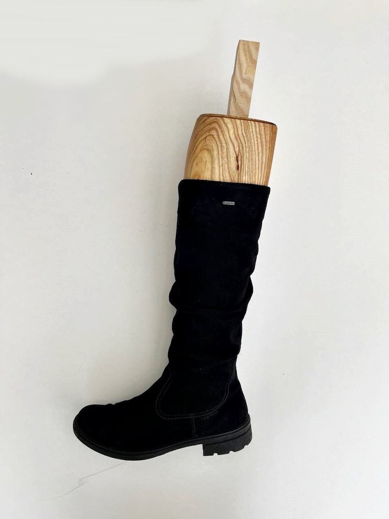 May include: A black suede knee-high boot with a wooden boot shaper inside. The boot has a low heel and a rounded toe.