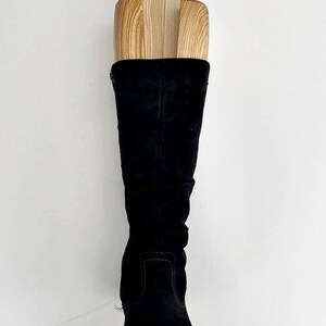 May include: A pair of black suede knee-high boots with a wooden boot shaper inside. The shaper is made of three pieces of wood.