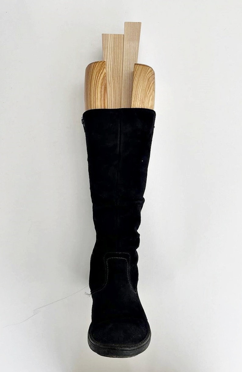 May include: A pair of black suede knee-high boots with a wooden boot shaper inside. The shaper is made of three pieces of wood.