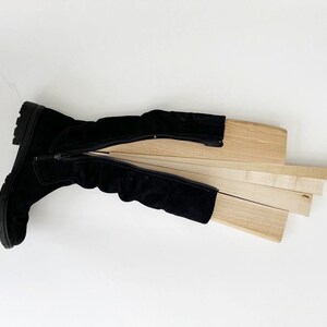 May include: A black suede boot with a zipper is open and laid flat. The boot is lined with wooden slats.