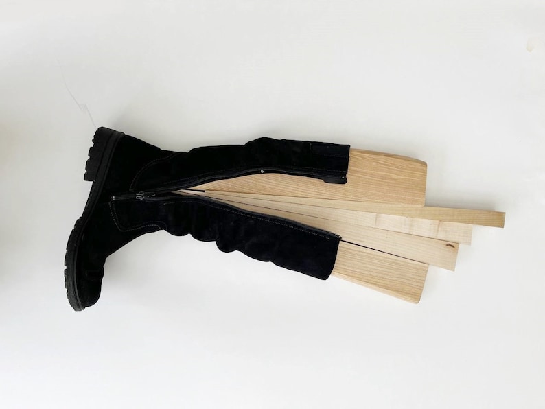 May include: A black suede boot with a zipper is open and laid flat. The boot is lined with wooden slats.