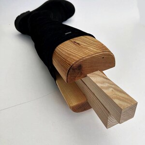 May include: A wooden boot stretcher with a black boot inserted. The stretcher is made of three pieces of wood, two of which are rectangular and one of which is curved. The curved piece of wood is inserted into the boot and the rectangular pieces are used to adjust the width of the stretcher.