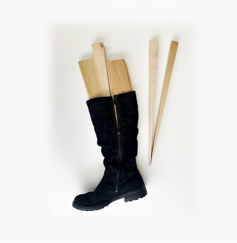 May include: A pair of black suede boots with a zipper up the back. Three wooden boot shapers are placed inside the boots.