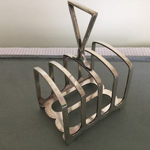 May include: Silver plated toast rack with a handle. The rack has five slots for holding toast.