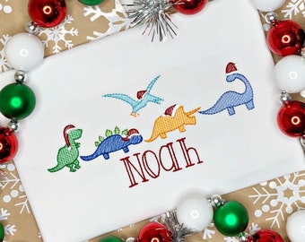 May include: White Christmas onesie with a red, green, blue, and orange embroidered design of dinosaurs wearing Santa hats. The onesie has the name "Noah" embroidered in red.