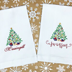 May include: Two white kitchen towels with embroidered Christmas trees and the names "Massingill" and "Swanson" in red cursive.