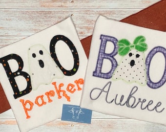 May include: Two white Halloween-themed shirts with the word "BOO" and ghost appliqués. One shirt has the name "Parker" in orange, the other has "Aubree" in cursive. The ghost has a black mouth and eyes.