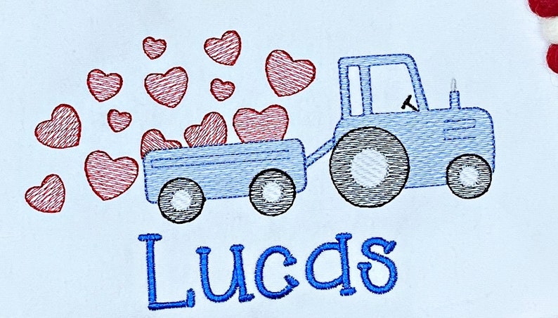 K&ouml;nnte beinhalten: Gesticktes Design eines blauen Traktors, der einen Wagen mit roten Herzen zieht. Der Name "Lucas" ist darunter in blauer Schrift gestickt. Das Design befindet sich auf wei&szlig;em Hintergrund.