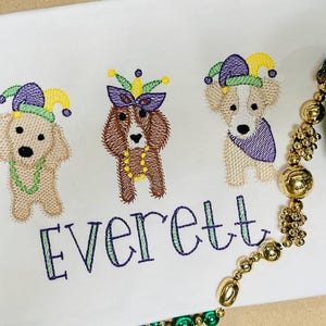 May include: Embroidered design of three dogs wearing Mardi Gras hats and beads. The name Everett is embroidered below the dogs.