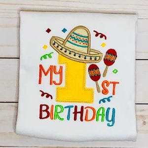 May include: A white onesie with colorful embroidery that says "My 1st Birthday". The number one is decorated with a brown sombrero and maracas.