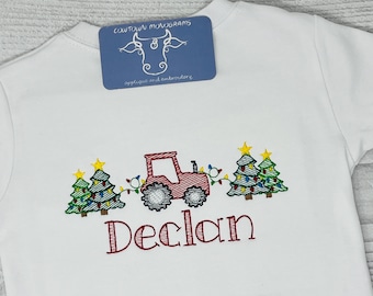 Puede incluir: Camiseta blanca de manga larga con bordado de tractor rojo y árboles de Navidad. El nombre "Declan" está bordado en rojo debajo. La camiseta tiene una etiqueta azul que dice "COWTOWN MONOGRAMS".