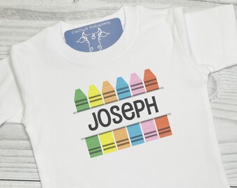 Könnte beinhalten: Weißes T-Shirt mit einem Design aus bunten Buntstiften und dem Namen "Joseph" in schwarzem Text.