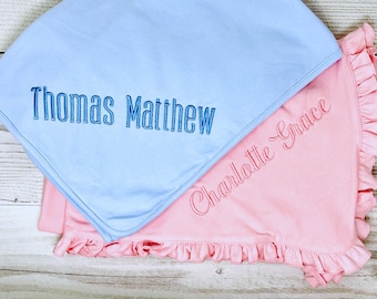 May include: Two baby blankets, one light blue and one pink, are displayed. The blue blanket has the name "Thomas Matthew" embroidered in blue. The pink blanket has the name "Charlotte Grace" embroidered in pink. Both blankets have a ruffled edge.