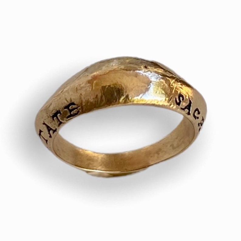 May include: A gold ring with a rounded top and the inscription "SACRE" on one side and "LATE" on the other.