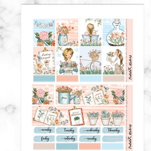 May include: A set of 12 planner stickers featuring floral illustrations, a bicycle, a watering can, a book, and a jar. The stickers are in shades of pink, blue, and green. The text on the stickers includes "Planting Journal", "Grow", "Year of Blessings", "Monday", "Tuesday", "Wednesday", "Thursday", "Friday", "Saturday", and "Sunday".
