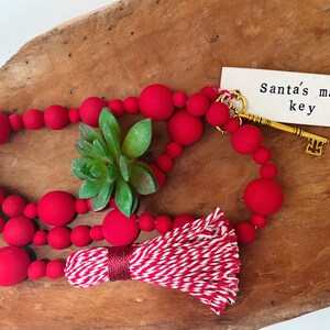 May include: Red beaded garland with a white and red striped tassel and a gold key with a tag that reads "Santa's magic key".