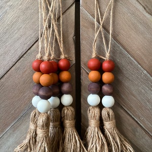 May include: Two fall-themed door hangers with brown, orange, and white wooden beads and a jute tassel.