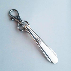 May include: A silver spoon keychain with a decorative design and a silver swivel clasp.