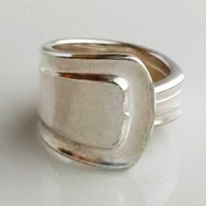 May include: A silver ring made from a recycled spoon. The ring is wide and has a unique, slightly curved design.