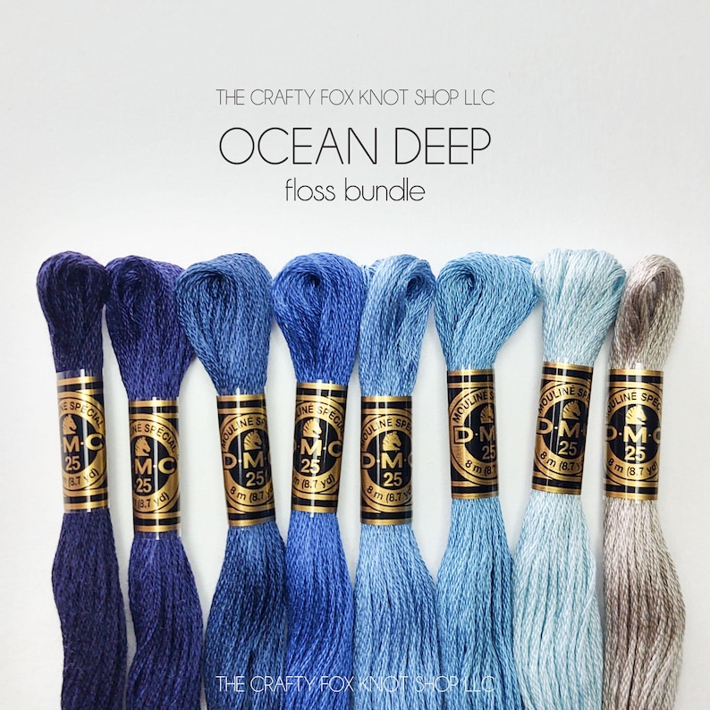 May include: A set of eight DMC embroidery floss spools in shades of blue, from dark navy to light blue, with a single spool of beige floss. The spools are labeled "DMC" and "Mouline Special" with the number "25" printed on each spool. The text "THE CRAFTY FOX KNOT SHOP LLC" and "OCEAN DEEP floss bundle" is printed above the spools.