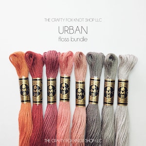 May include: A set of eight embroidery floss spools in shades of orange, red, pink, gray, and beige. The spools are labeled "DMC" and "Special" with the number "25". The text "The Crafty Fox Knot Shop LLC" and "Urban floss bundle" is printed above the spools.