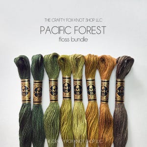May include: A set of eight DMC embroidery floss spools in shades of green, yellow, and brown. The spools are labeled "DMC" and "25". The text "PACIFIC FOREST floss bundle" is displayed above the spools.