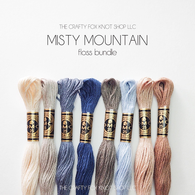 May include: A set of eight embroidery floss spools in various shades of beige, blue, and brown. The spools are labeled "DMC" and "25". The text "Misty Mountain floss bundle" is displayed above the spools.
