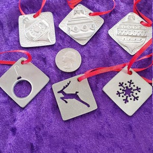 May include: A collection of silver-colored Christmas ornaments with red ribbons. The ornaments have various designs, including a snowflake, a reindeer, and a Christmas ball. A US quarter is also present.