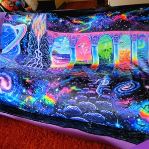 May include: A colourful, psychedelic blanket depicting a cosmic scene with galaxies, planets, and an astronaut. The design includes arches, a waterfall, and a path through the cosmos. The blanket is mainly black with bright, neon colours, creating a vibrant visual.
