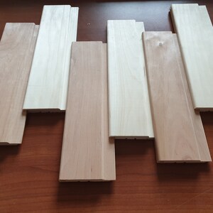 May include: A set of six wooden wall panels, three are light brown and three are a lighter shade of wood. The panels have a slightly raised edge around the perimeter.