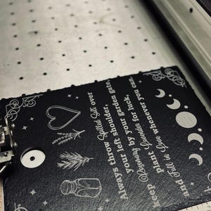 May include: Black slate sign with white text and illustrations. The text reads "Always throw Spilled Salt over your left shoulder, keep Rosemary by your garden gate, plant Lavender for luck, and Fall in Love whenever you can."