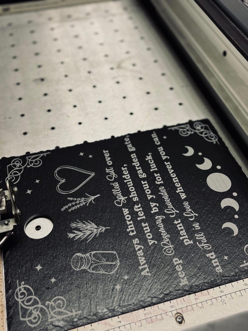 May include: Black slate sign with white text and illustrations. The text reads "Always throw Spilled Salt over your left shoulder, keep Rosemary by your garden gate, plant Lavender for luck, and Fall in Love whenever you can."