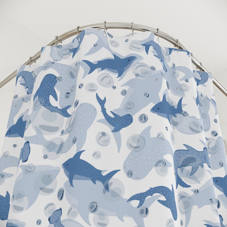 Pu&ograve; includere: Tenda da doccia bianca con un motivo di squali e bolle blu. Gli squali variano per dimensioni e stile, alcuni con motivi a pois. La tenda &egrave; appesa a un'asta metallica curva, creando un angolo. Il design &egrave; giocoso e acquatico.