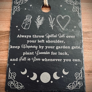 May include: Black slate sign with white text and illustrations. The text reads "Always throw Spilled Salt over your left shoulder, keep Rosemary by your garden gate, plant Lavender for luck, and Fall in Love whenever you can."