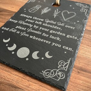 May include: Black slate sign with white text and illustrations. The text reads: "Always throw Spilled Salt over your left shoulder, keep Rosemary by your garden gate, plant Lavender for luck, and Fall in Love whenever you can."