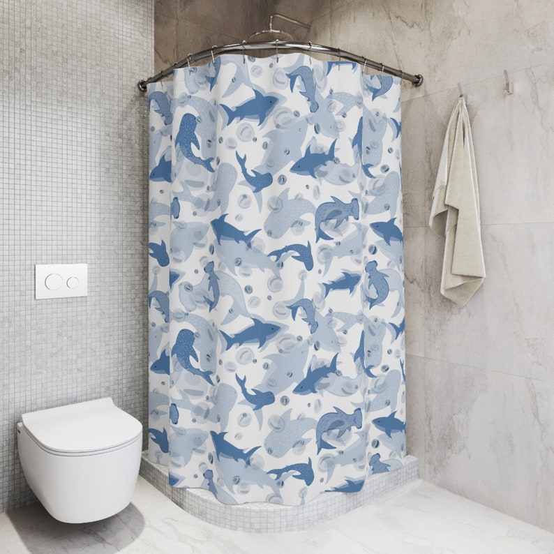 Pu&ograve; includere: Tenda da doccia bianca con un motivo ripetuto di squali e bolle blu. Gli squali variano per dimensioni e tonalit&agrave;, creando un tema acquatico e giocoso. La tenda &egrave; in un bagno.