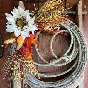 May include: A rustic fall wreath made with a rope circle, white sunflower, dried grasses, and fall leaves.