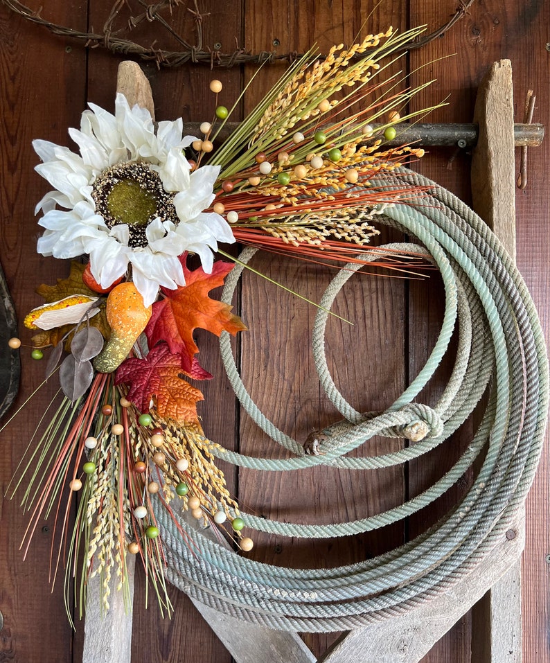 May include: A rustic fall wreath made with a rope circle, white sunflower, dried grasses, and fall leaves.