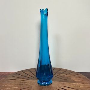 May include: A tall, slender, blue glass vase with a ruffled top and a flared base. The vase has a textured, rippled surface.