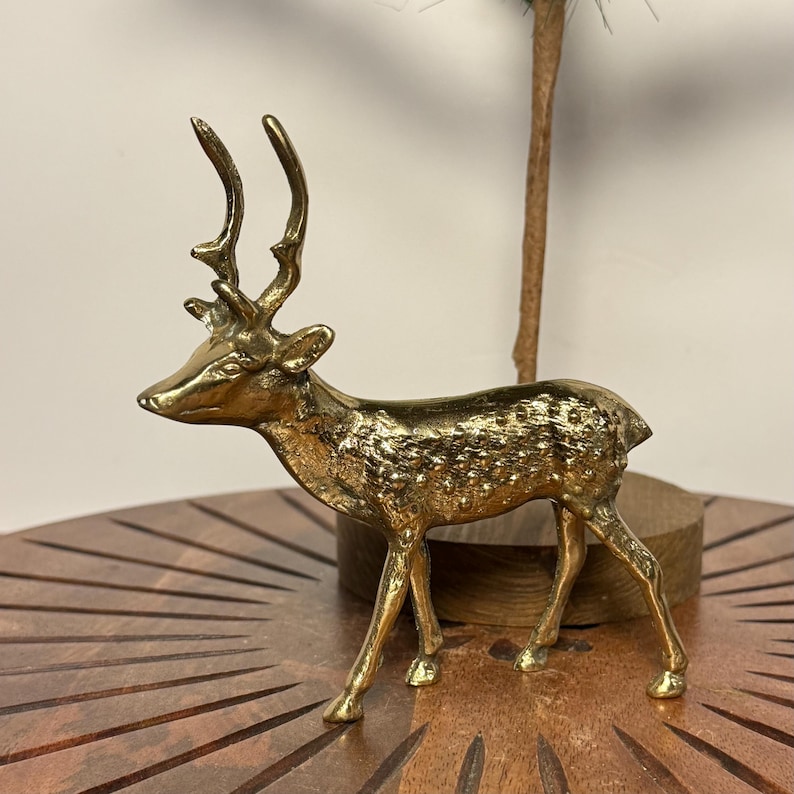May include: A golden-colored deer figurine with detailed antlers and textured body. The deer is posed in a standing position, showcasing its elegant form. This decorative item is likely made of metal and is suitable for home decor.