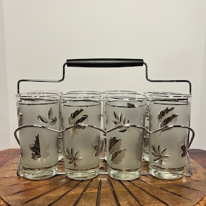 May include: A set of six frosted glass tumblers with a silver leaf design, in a chrome wire holder with a black handle.