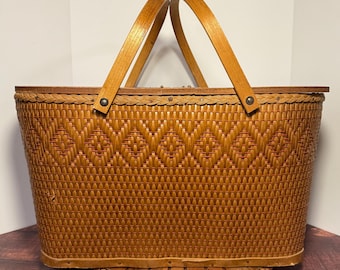 May include: A vintage picnic basket with a woven brown exterior and wooden handles. The basket features a diamond pattern and is set on a wooden base. The handles are arched and attached with metal rivets.