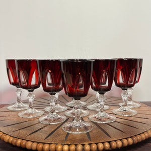 May include: Set of ten red wine glasses with clear stems and bases. The glasses are arranged in a circle on a wooden surface.
