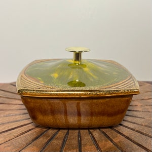 May include: A square ceramic dish with a lid. The dish is brown with a green and yellow glaze. The lid has a gold knob.