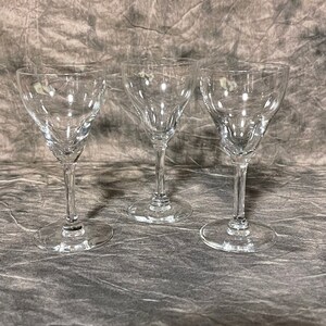 May include: Three clear, stemmed glasses with a tulip-shaped bowl and a slender stem. The glasses are made of transparent glass and are arranged in a row, showcasing their elegant design. The glasses are suitable for serving wine or other beverages.