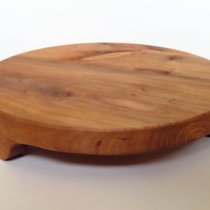 May include: A round wooden serving tray with a natural wood finish and three legs. The tray is made of solid wood and has a smooth surface.