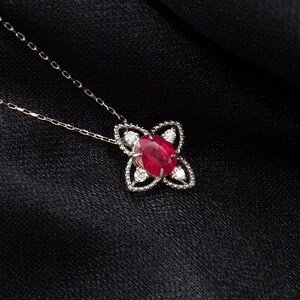 以下が含まれることがあります： 銀色のチェーンネックレスに、赤いルビーの宝石が銀の花のデザインでセットされたペンダントがついた、繊細なネックレスです。