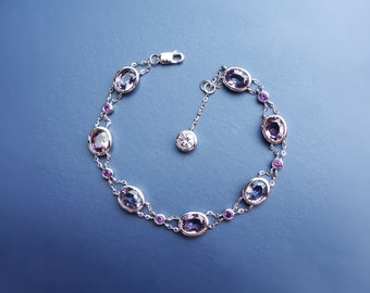 Può includere: Un braccialetto d'argento con una doppia fila di pietre ovali. Le pietre sono un mix di viola, rosa e trasparente. Il braccialetto ha un piccolo ciondolo rotondo di pietra trasparente.