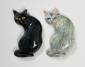 May include: Two ceramic cat figurines, one black and one white, with painted details. Both cats are curled up in a sitting position.