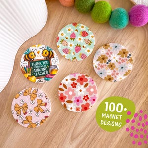May include: A selection of circular magnets with diverse patterns. One magnet has bees and the text "Thank you for being an amazing teacher." Other magnets show floral, strawberry, and bow designs. The image also includes a green oval with the text "100+ Magnet Designs."